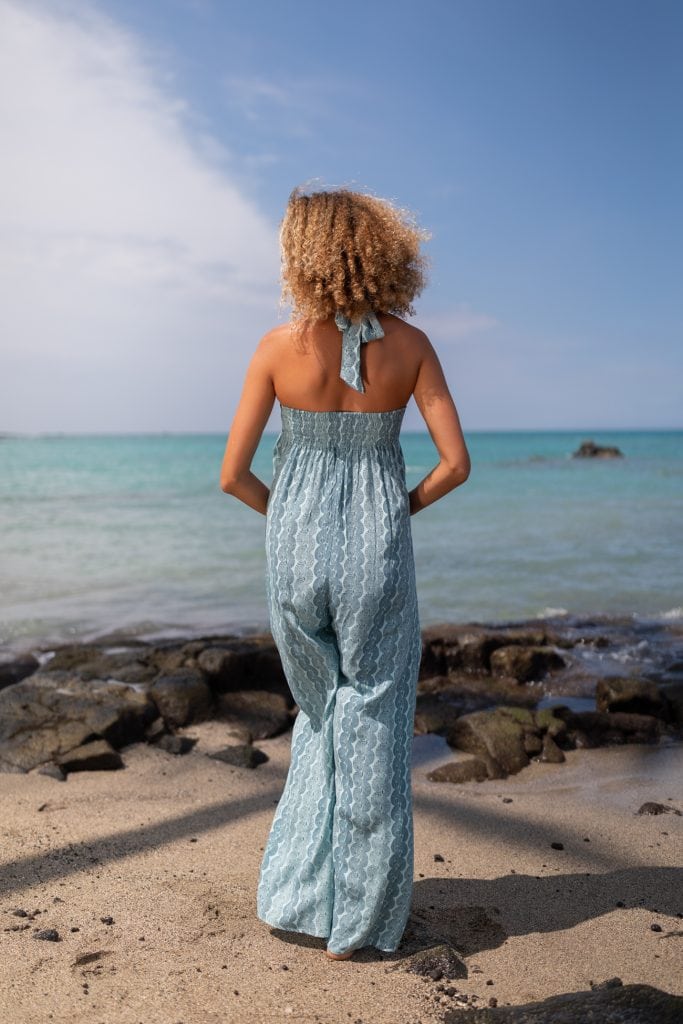 Female model wearing Kaihawanawana Jumpsuit in a Lei Kupee Print and Blue Tint/Real Teal Color - Back View