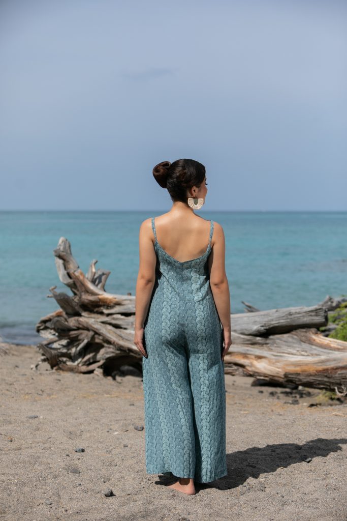 Female model wearing a Lanihau Jumpsuit in Lei Kupee Print and Real Teal/Blue Tint Color - Back View