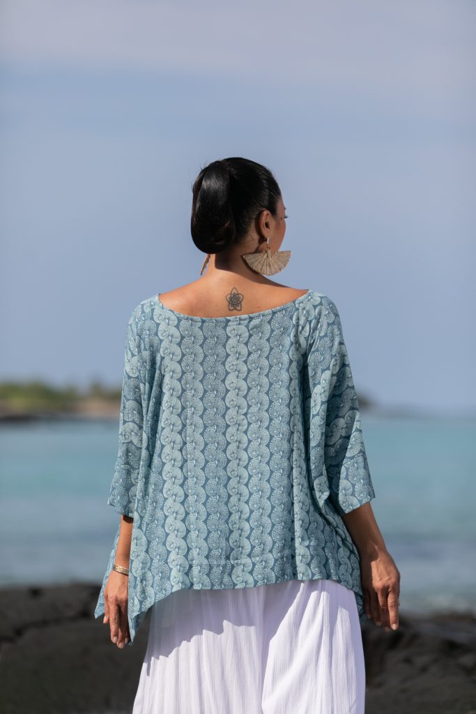 Female model wearing a Puako Top in Lei Kupee Print and Real Teal/Blue Tint Color - Back View